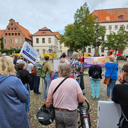 Menschen stehen bei einer Kundgebung für Integration und Zusammenhalt in einer Stadtansicht mit historischen Gebäuden.