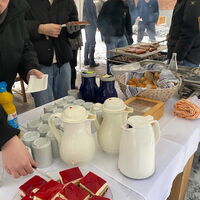 Auf einem Tisch stehen Kannen und Kuchen bereit, während Menschen von der Hauswirtschaft des Wichernhauses versorgt werden.