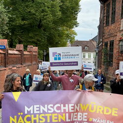 Menschen demonstrieren für seelische Gesundheit und Zusammenhalt mit Plakaten in einer Stadtstraße.
