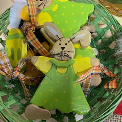 Ein bunter Korb mit handgemachten Holzfiguren in Hasenform, die fröhlich in grünen Kleidern arrangiert sind.