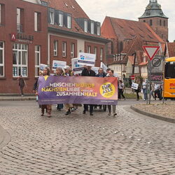 Eine Gruppe von Menschen marschiert mit einem Banner für Menschenwürde und Zusammenhalt durch die Stadt.