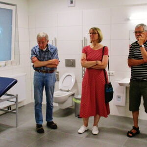 Eine Gruppe von fünf Personen hört einem Mann in einem modernen Raum mit Toilettenanlage aufmerksam zu.