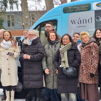Eine Gruppe von Menschen freut sich über ein neues, blaues Fahrzeug mit Werbelogos im verschneiten Freien.