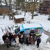 Eine Gruppe von Werbepartnern steht fröhlich vor einem neuen, bunt beklebten Fahrzeug im verschneiten Winter.