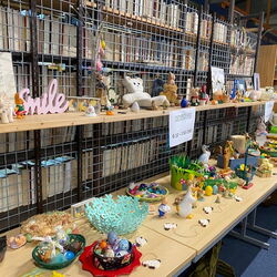 Bunte Osterdekorationen und Sammlerstücke sind auf einem Tisch ausgestellt, umgeben von Regalen voller Bücher.