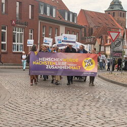 Eine Gruppe von Menschen marschiert mit einem Banner für Menschenwürde und Zusammenhalt durch die Straßen.