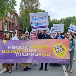 Menschen demonstrieren für Nächstenliebe und Zusammenhalt mit Plakaten in einer lebhaften Straßenumgebung.