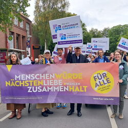 Demonstration für Menschenwürde und Nächstenliebe, Teilnehmer halten Banner und Schilder in einer belebten Straße.