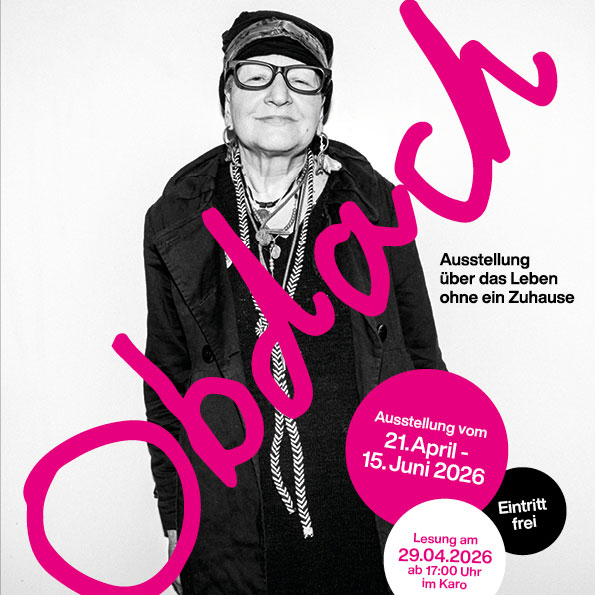 Eine ältere Frau steht selbstbewusst vor einem Plakat der Ausstellung „Obdach“ über das Leben ohne Zuhause.
