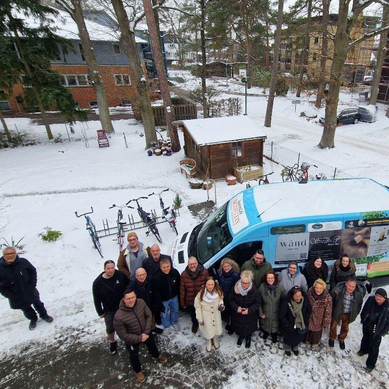 Eine Gruppe von Menschen steht freudig vor einem mit Werbung beklebten Fahrzeug im verschneiten Außenbereich.
