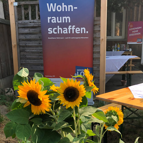 Bild eines Plakats "Wohnraum schaffen" mit Sonnenblumen im Vordergrund