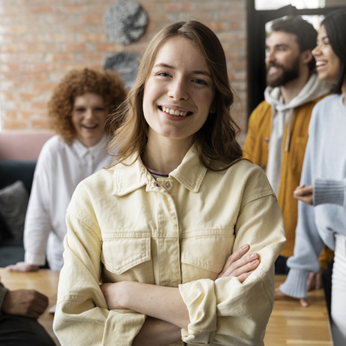 Gruppe von Menschen im Hintergrund, im Vordergrud steht eine sympathische Person und schaut ins Bild