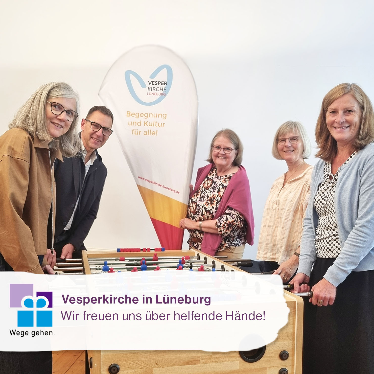 Personen aus dem Planungsteam der Vesperkirche kickern, davor Hinweis auf Ehrenamtgesuch